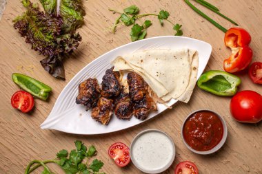 Sebze ve otlarla dolu beyaz bir tabakta pide ekmekli ciğer kebabı..