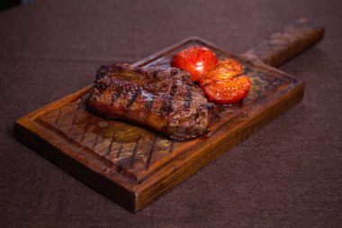 Lezzetli bir biftek, mükemmel ızgara, ahşap bir tahtada domateslerle servis ediliyor. Lezzetli bir öğle ya da akşam yemeği için ideal..