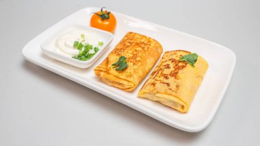 Two folded stuffed savory crepes with sour cream and chives garnish on a white plate on a white background. clipart