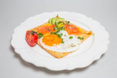 Close-up shot of a crepe with smoked salmon, avocado, egg, and tomatoes on a white plate. Square shape, elegant presentation. clipart