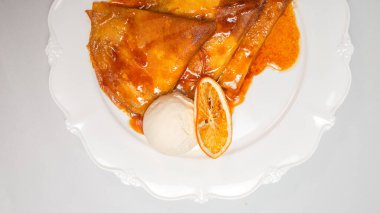 Üzerinde portakal sosu ve beyaz arka planda izole edilmiş bir top vanilyalı dondurma olan bozulmuş bir krep tatlısı..