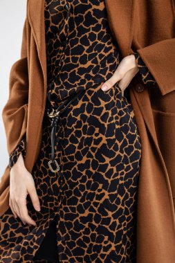 Tarz sahibi genç bir kadın, modaya uygun kahverengi bir ceket ve şık bir hayvan desenli elbise içinde, zarif ve modern bir şekilde poz veriyor..