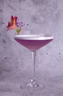 Gri bir arka planda çiçek süslemesi olan pembe bir kokteylin zarif bir görüntüsü..