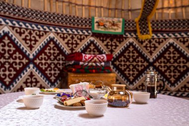 Yurdun içinde, içinde fincanlar, tabaklar ve yiyecekler olan bir masa hazırlanır. Renkli halılar ve halılar mekanı süslüyor..