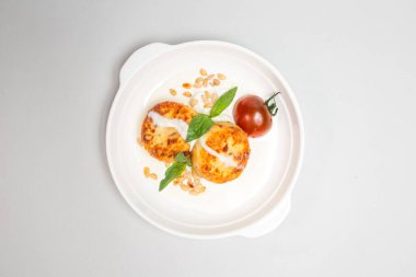 Beyaz arka planda beyaz bir tabakta ekşi kremalı ve vişneli domatesli iki yuvarlak peynirli krep. Beyaz bir arkaplanda izole edilmiş.