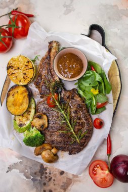 Sulu ve yumuşak ızgara biftek çeşitli kızarmış sebzelerle servis edilir ve üzeri biberiye dalıyla kaplanır..