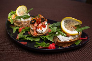 Krem peynirli, domatesli, zeytinli, siyah tabakta limonlu, marullu ve zencefilli çeşitli bruschetalar.