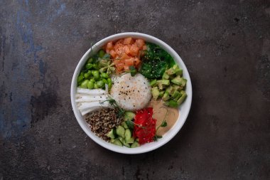 Beyaz tabakta somon, avokado, salatalık, lahana, pirinç ve susam içeren sağlıklı dürtme kabı için taze malzemelerin üst görüntüsü.