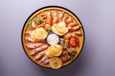 A delicious and fresh seafood platter with various types of shrimps, lemon wedges, and potato chips, served on a wooden board. clipart