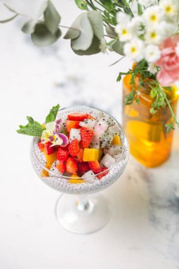 Çilekli Chia tohumu pudingi, mango, mermer masada cam içinde ejderha meyvesi. Sağlıklı vejetaryen kahvaltısı veya atıştırmalık.