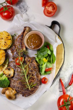 Sulu ve yumuşak ızgara biftek çeşitli kızarmış sebzelerle servis edilir ve üzeri biberiye dalıyla kaplanır..