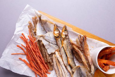 Çeşitli kurutulmuş balıklar, havuçlar ve balkabağı dilimleri gri arka planda beyaz bir kağıtta. Gri bir arkaplanda izole edilmiş.