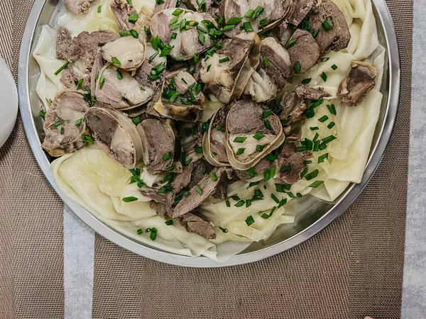 stock image The Kazakh national dish is beshbarmak. thinly sliced beef and lamb on a large round plate with dough