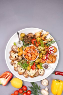 Beyaz tabakta çeşitli et, sebze ve aperatifler var. Boş alana sahip gri arkaplan, metin, menü veya yemek reklamı için mükemmel.