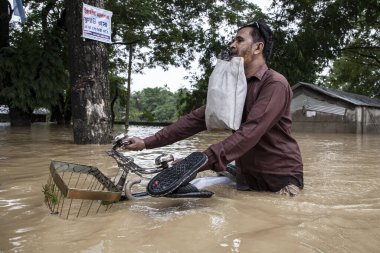 9 Ağustos 2023 'te Güney Chittagong, Bangladeş' ten Satkania Upazila 'da göğüs ve bel seviyesindeki suyla dolu yol boyunca yayalar, kamyonlar ve bisikletler yürüyor..