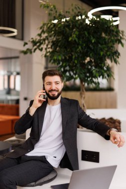 Ofiste cep telefonuyla konuşan mutlu bir iş adamı. İş adamı profesyonel yönetici elinde akıllı telefon ile müşteriyle iletişim kuruyor..