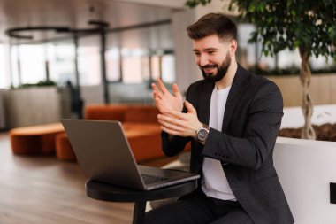 Girişimci iş başarısından sonra alkışlıyor, modern ofiste dizüstü bilgisayarla çalışıyor.