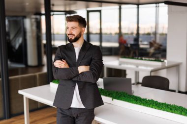 Resmi gömlekli, elleri katlı ve dişlek bir gülümsemeyle kameraya bakan yakışıklı bir yönetmen. Neşeli iş profesyoneli, yönetici, girişimci portresi