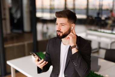 İş yerindeki mutlu iş adamı kulaklık takıyor, cep telefonu kullanıyor, gülümsüyor, akıllı telefondan sanal cep telefonu görüşmesi yapıyor, maç izliyor..