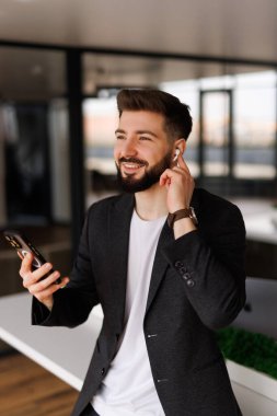 İş yerindeki mutlu iş adamı kulaklık takıyor, cep telefonu kullanıyor, gülümsüyor, akıllı telefondan sanal cep telefonu görüşmesi yapıyor, maç izliyor..