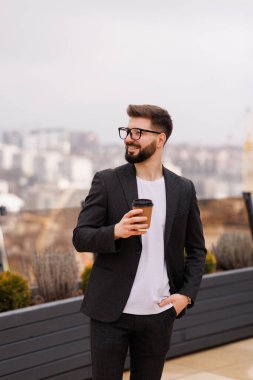 Biraz ara ver. Ofis balkonunda kahve molası verirken gülümseyen iş adamının belini kaldırın.