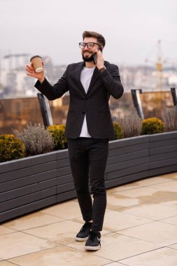 Ofiste kahve fincanı içen gülümseyen işadamı modern işyerinde dururken pencereden bakıyor.