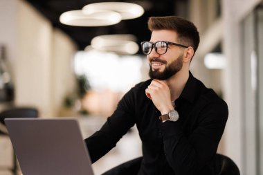 Modern ofis ortamında masa başında çalışan odaklanmış bir iş adamı. Konsantrasyonunu ve kendini bilgisayardaki görevlere adamış. Kurumsal çalışma ortamlarını resmetmek için ideal.