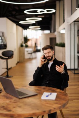 Gülümseyen adam telefon ederken notlar yazıyor ve evde dizüstü bilgisayar kullanıyor.