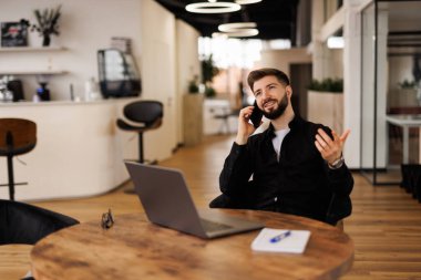 Şirket iletişimi. Uzaktan çalışan, mali belgeleri okuyan, cep telefonuyla konuşan, ofis içlerinde masa başında oturan mutlu bir erkek yönetici.