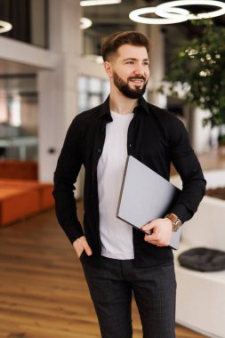 Erkek profesyonel dizüstü bilgisayarla çalışıyor ve ofis koridorunda kendinden emin bir şekilde başka tarafa bakıyor.