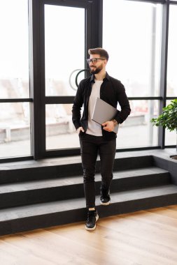 Erkek profesyonel dizüstü bilgisayarla çalışıyor ve ofis koridorunda kendinden emin bir şekilde başka tarafa bakıyor.