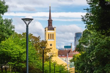 St. Johns Kilisesi sarı kulesi, Tallinn, Estonya 'da tarihi ve modernliği harmanlayan bulutların ve modern gökdelenlerin olduğu yemyeşil ağaçların arasında yer alıyor..