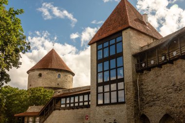 Danimarka Kralları Bahçesi, Tallinn, Estonya 'da kırmızı kiremitli çatıları ve tarihi taş duvarları olan ortaçağ kuleleri parlak mavi gökyüzü ve bulutlarla dolu güneşli bir günde ele geçirildi..