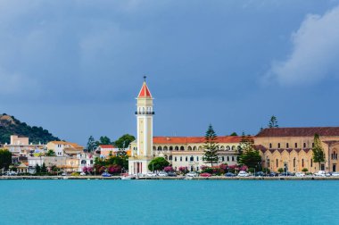 Aziz Dionysios Kilisesi 'nin çan kulesi Yunanistan' ın Zakynthos kentindeki renkli deniz kenarındaki binaların üzerinde yükselir. Turkuaz deniz, kasvetli ve fırtınalı gökyüzü ile çelişiyor..