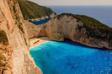 Zakynthos 'taki Navagio sahilinin nefes kesici hava manzarası, ikonik gemi enkazı, canlı turkuaz sular, beyaz uçurumlar ve kıyıya ulaşan turistik botlar.