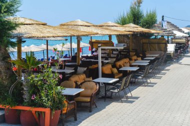 Limenaria, Thasos, Yunanistan 'daki deniz kenarı kafe. Güneşli bir günde mavi denize bakan boş masalar, saman şemsiyeler ve yaz atmosferi..