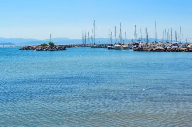 Yunanistan 'ın Patras kentindeki Theatraki yakınlarındaki marinaya yanaşmış yelkenlilerin sakin bir yaz manzarası. Temiz turkuaz su, uzak dağlar ve huzurlu bir atmosfer..
