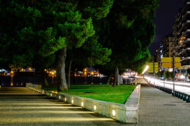 Yunanistan 'ın kuzeyindeki Beyaz Kule' nin altında çekilen ağaçlar, aydınlık kaldırımlar ve sokak lambaları ile Selanik rıhtımının gece görüşü.