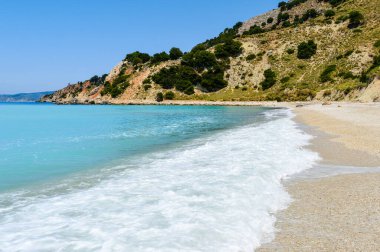 Yunanistan 'ın Kefalonia kentindeki Zola yakınlarındaki Agia Kyriaki sahiline ulaşan dalgalar. Berrak turkuaz su, yumuşak dalga köpüğü ve yaz güneşinde doğal uçurumlar.