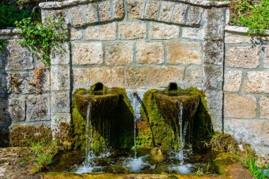 Yunanistan 'ın Trikala kentinde yosun ve akan suyla geleneksel taştan bir çeşmenin simetrik manzarası. Doğal dokular ve gündüz detayları.