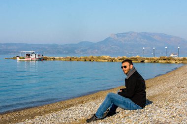 Yunanistan 'ın Corinth kentindeki Kato Assos kıyı köyünde gelişigüzel oturan genç bir adam görülüyor. Rahat bir yolculuk atmosferi, doğal ışık ve huzurlu bir sahil havası..