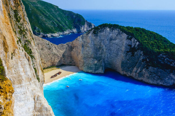 Потрясающая широкоугольная фотография знаменитого пляжа Наваджио в Закинфе, Греция, с кораблекрушением на золотом песке, бирюзовом море, туристических лодок и драматических скал.