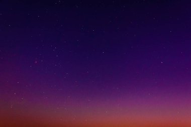 Yıldızlarla dolu gece gökyüzü turuncu ve mor renklerin değişken bir karışımı. Soyut kullanım, arka plan veya yaratıcı tasarım için temiz ve canlı bir çekim ideali.