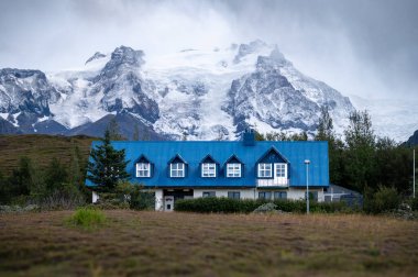 Dağlarda bir ahşap kulübe. Karla kaplı ağaçlar ve İzlanda 'da bulutlu bir gökyüzü.