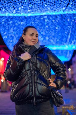 Gece bir caddenin üzerinde asılı duran parlak mavi LED sicim ışıkları altında duran bir kadın portresi. Sahne, Belçika 'nın Mons şehrinde aydınlık bir şehrin büyülü atmosferini yakalıyor.