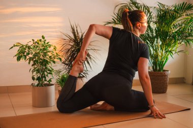 Yogi sportif çekici kadın yoga, yoga-asana pozu ve meditasyon yapıyor, yalnız çalışıyor, esniyor, şık siyah spor giysiler giyiyor, kapalı yeşil ev bitkileri arasında.