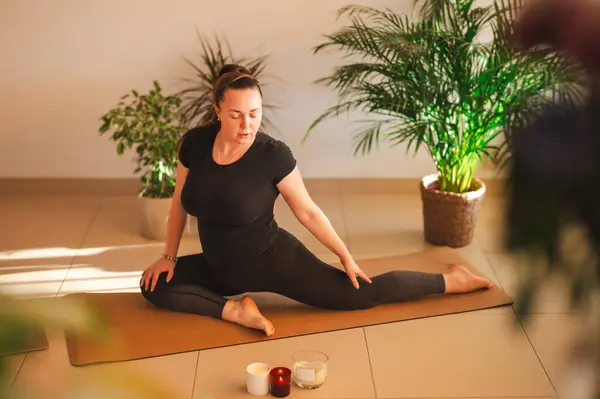 Yogi sportif çekici kadın yoga, yoga-asana pozu ve meditasyon yapıyor, yalnız çalışıyor, esniyor, şık siyah spor giysiler giyiyor, kapalı yeşil ev bitkileri arasında.