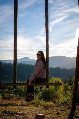 Tek başına bir gezgin, görkemli dağlar ve altın bir günbatımıyla çevrili dev bir ahşap salıncakta huzurlu bir anın tadını çıkarır. Özgürlüğü kucaklamak ve doğayla bağ kurmak için mükemmel bir yer..