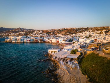 Mykonos Eski Kasabası 'nın ikonik beyazlatılmış evleri, tarihi yel değirmenleri ve canlı limanlarıyla baş döndürücü hava günbatımı manzarası. Ege Denizi 'nin altın rengi büyülü ada atmosferine eklenir.