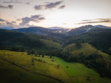 Gün batımında dağlık kırsal bir manzara. Uzak vadinin üstündeki dramatik gökyüzü. Tepedeki yeşil tarlalar ve ağaçlar. Karpatların güzel doğa manzarası. Yüksek kalite fotoğraf
